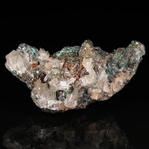 May include: A close-up of a mineral specimen featuring clear, crystalline formations and a mix of green, brown, and white hues. The mineral has a rough, textured surface and is set against a black background.