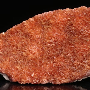 May include: A large, orange-red mineral specimen with a rough, textured surface. The mineral is composed of many small, needle-like crystals.