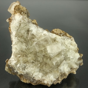 May include: A cluster of clear, translucent crystals on a brown, rocky matrix. The crystals are arranged in a random pattern and have a slightly iridescent sheen.
