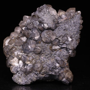 Könnte beinhalten: Ein Cluster aus klaren, glasartigen Quarzkristallen auf einer dunkelgrauen, metallischen Matrix. Die Kristalle sind scharf und gut ausgebildet, mit einer Vielzahl von Größen und Formen.