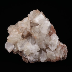 May include: A cluster of crystalline minerals with a mix of translucent and opaque sections. The crystals are primarily off-white with hints of brown and tan, set against a black background. The mineral formation has a rough, textured appearance.