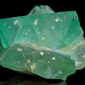 May include: A cluster of green fluorite crystals with a glassy luster. The crystals are intergrown and have a variety of shapes and sizes. The fluorite is translucent and has a light green color.