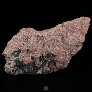 May include: A large, rough, pink and black rock with a crystalline texture. The rock has a natural, irregular shape and is covered in small, sparkling crystals.