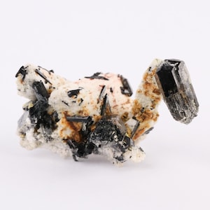 May include: A cluster of black tourmaline crystals embedded in a matrix of white, tan, and light pink minerals. The crystals are sharply defined and contrast with the lighter-colored host rock. The overall appearance is rough and natural.