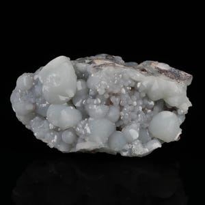 May include: A light blue mineral specimen with a bubbly, rounded texture. The surface is covered in small, spherical formations, with larger, smooth, rounded shapes interspersed throughout. The mineral sits against a black background.