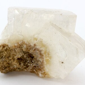 May include: A clear, translucent crystal with a rough, brown base. The crystal has a geometric shape with sharp edges and appears to be a natural mineral specimen.