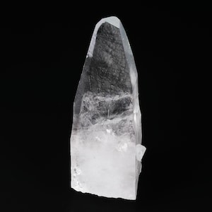 May include: A clear quartz crystal with a pointed tip. The crystal is transparent with internal fractures and inclusions, set against a black background. The crystal's base is a milky white color.