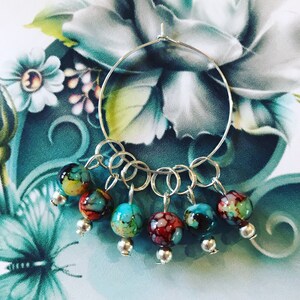 May include: A silver hoop earring with seven colourful glass beads hanging from it. The beads are a mix of blue, green, red, and yellow.
