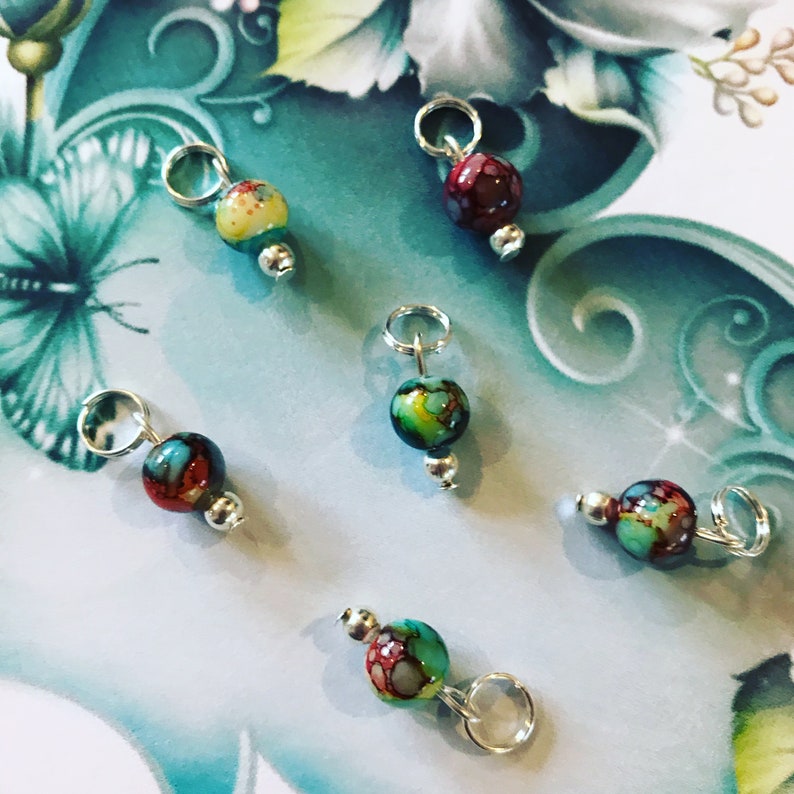 May include: Six colourful glass beads with silver jump rings. The beads are a mix of red, green, yellow, and blue.