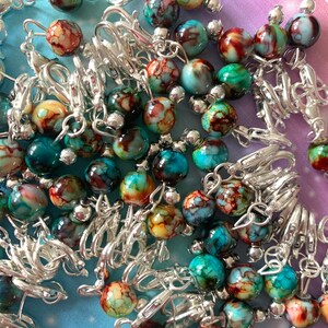 May include: A close-up of a pile of colourful, marbled glass beads with silver metal clasps. The beads are a mix of blue, green, and brown with white swirls.