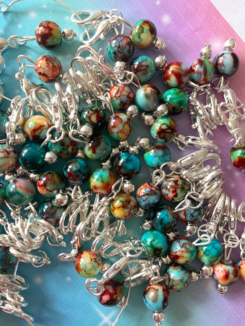May include: A close-up of a pile of colourful, marbled glass beads with silver metal clasps. The beads are a mix of blue, green, and brown with white swirls.