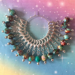 May include: A silver ring with 18 turquoise and brown marbled beads attached to it. The beads are connected to the ring with silver jump rings.
