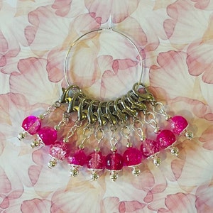 May include: A silver hoop with a series of pink glass beads hanging from it. The beads are clear with pink flecks and are attached to the hoop with silver rings.