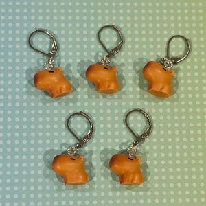 May include: Five silver capira charms with brown capybara heads. The charms are attached to silver jump rings.