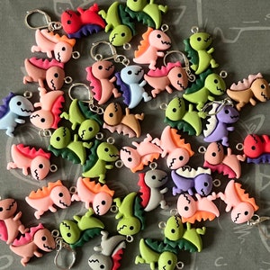 May include: A collection of colorful plastic dinosaur charms with various colors and designs. The charms are perfect for adding a playful touch to jewelry, keychains, or other crafts.