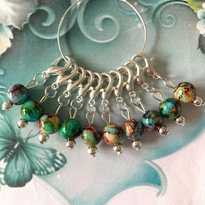 May include: A silver ring with 10 colourful glass beads attached. The beads are a mix of blue, green, and brown.