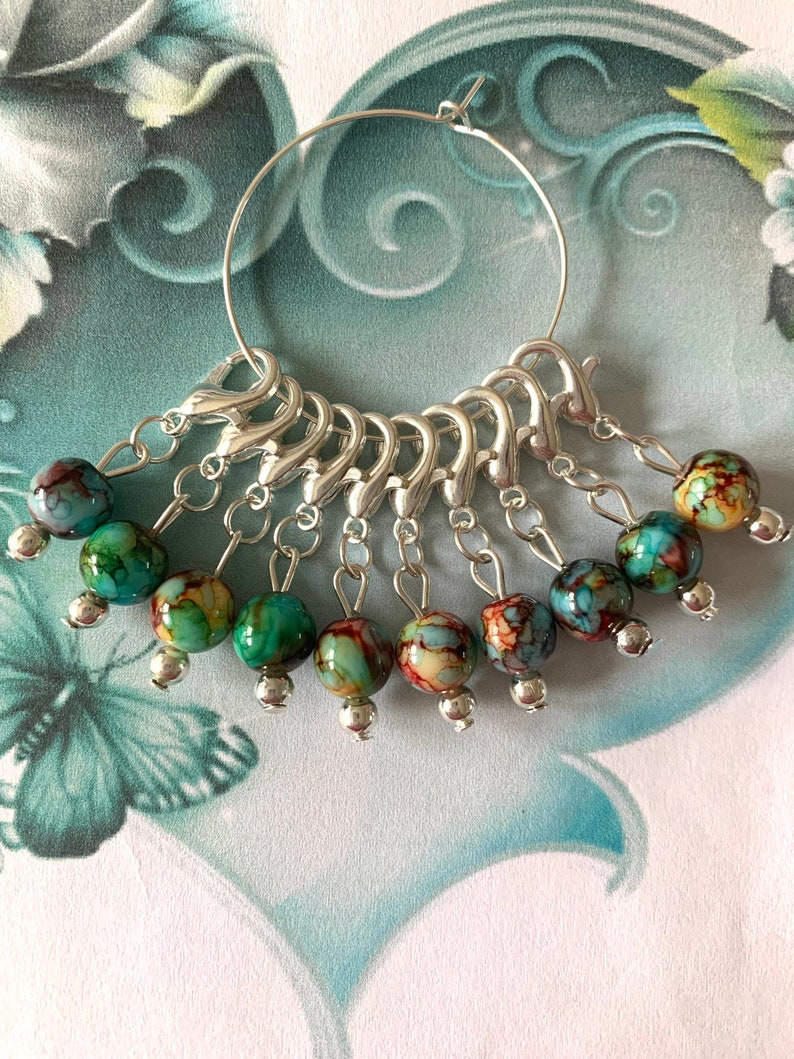 May include: A silver ring with 10 colourful glass beads attached. The beads are a mix of blue, green, and brown.