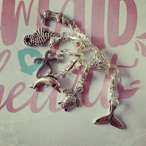 May include: A silver charm bracelet with a variety of charms, including a seahorse, a starfish, a dolphin, a turtle, and a heart. The charms are attached to a silver chain with a lobster clasp.