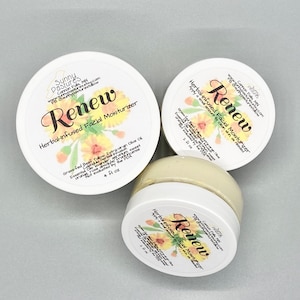 May include: Three white-lidded jars of "Renew" herbal-infused facial moisturizer. The labels feature floral designs and text, including the brand name "Sunny Pastures." The jars contain a creamy, yellow product. One jar is open, revealing the moisturizer.