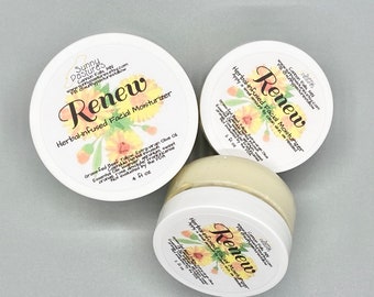Puede incluir: Tres tarros con tapa blanca de crema hidratante facial herbal "Renew". Las etiquetas presentan diseños florales y texto, incluido el nombre de la marca "Sunny Pastures". Los tarros contienen un producto cremoso y amarillo. Un tarro está abierto.