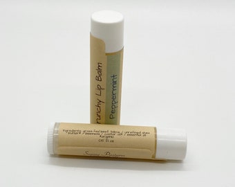 Puede incluir: Dos tubos de bálsamo labial marrón y blanco con una etiqueta que dice "Crunchy Lip Balm Peppermint" e "Ingredientes: sebo de res alimentado con pasto / manteca de karité sin refinar / cera de abejas / aceite de ricino / aceite esencial #orgánico 0.15 fl oz Sunny Pastures".