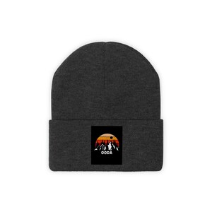 May include: Dark gray beanie with a rectangular patch featuring a sunset design over a mountain range. The patch includes the word "OODA" in white. The beanie is a winter accessory.