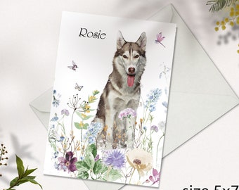 Könnte beinhalten: Eine personalisierte Grußkarte mit einer Aquarell-Illustration eines Husky-Hundes mit blauen Augen und einer rosa Zunge, umgeben von bunten Wildblumen und Schmetterlingen. Die Karte ist weiß mit dem Namen "Rosie" in Schwarz obenauf gedruckt.