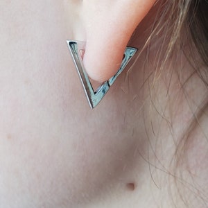 May include: Silver triangle hoop earrings. The earrings are in the shape of a triangle with a small opening at the top.