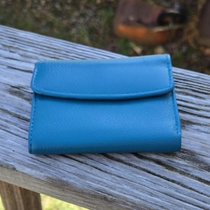 May include: A small, turquoise leather wallet with a flap closure. The wallet is rectangular and appears to be made of textured leather. The stitching is visible around the edges of the wallet.