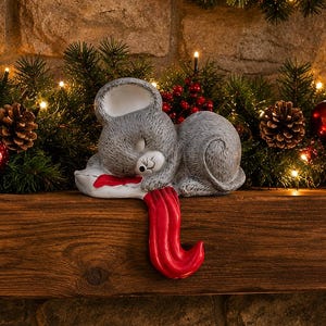 May include: A gray ceramic mouse figurine sleeping on a white pillow with a red trim. The mouse has closed eyes, a small black nose, and whiskers. A long, smooth, bright red tail extends from the pillow, curving downward over the edge.