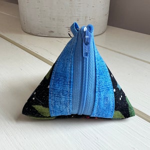May include: A small triangular zippered pouch with a blue zipper and a black fabric with a green and white floral pattern.