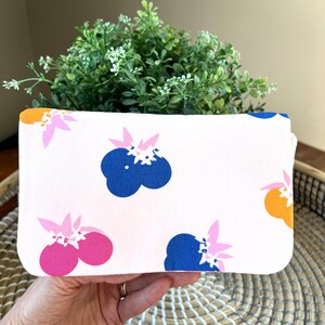 Puede incluir: Una bolsa de tela blanca con un estampado floral rosa, azul y naranja. La bolsa está hecha de una tela de algodón suave y tiene un cierre de cremallera.