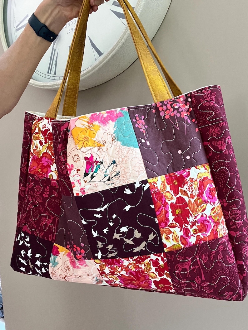 Peut inclure: Grand sac fourre-tout patchwork avec des carr&eacute;s de tissu &agrave; motifs floraux et d'oiseaux dans les tons bordeaux, rose, jaune et turquoise. Le sac a des anses en cuir couleur moutarde.