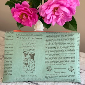 May include: A rectangular zippered pouch in light green fabric featuring a printed excerpt from the book Rose in Bloom by Louisa M. Alcott. The text is in black, accompanied by a vintage-style illustration of a person in a dress and hat.
