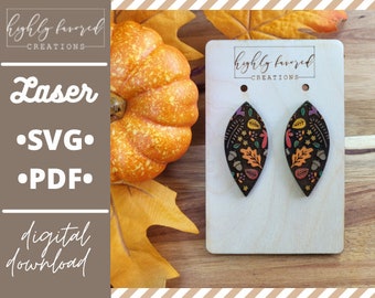 May include: A pair of laser cut wooden earrings with a fall-themed design. The earrings are shaped like leaves and feature a variety of colors, including red, orange, yellow, green, and brown. The earrings are on a white card with the text "highly favored creations" printed on it.