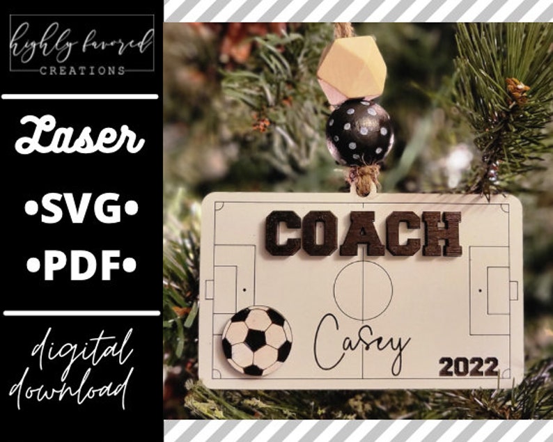 May include: A white wooden ornament shaped like a soccer field with a black soccer ball, the word "COACH" in black letters, and the text "Casey 2022".