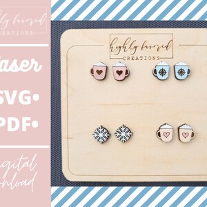 May include: A wooden board displaying six laser cut wooden earrings. The earrings are shaped like mugs with various designs. There are two mugs with snowflakes, two mugs with hearts, and two mugs with whipped cream and hearts. The board features the text "highly favoured -CREATIONS- " printed on it.