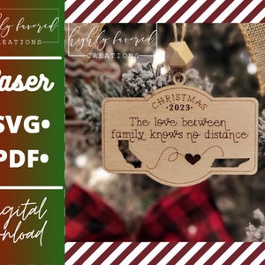 Może przedstawiać: Drewniana ozdoba choinkowa z napisem "CHRISTMAS 2023 - The love between family knows no distance" i zarysowaniem stanu Kalifornia. Ozdoba jest zawieszona na choince.