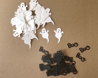 May include: White paper ghost cutouts and black paper "Boo" cutouts. The ghosts are in a pile and the "Boo" cutouts are scattered on a brown surface.