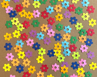 May include: A collection of colorful paper flower cutouts in various shades of red, orange, yellow, green, blue, and purple. The flowers are scattered on a brown background.