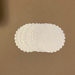 May include: A stack of white scalloped paper circles, perfect for crafting or scrapbooking.
