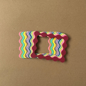 May include: A rectangular, layered paper frame with a wavy edge. The frame features a vibrant array of colors, including pink, yellow, blue, and purple. The outer frame is a deep red color, creating a striking contrast against the colorful interior.