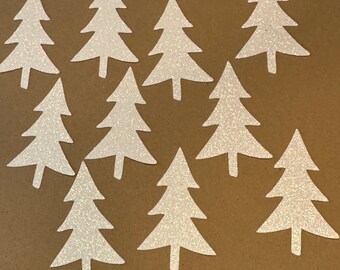 May include: Ten white glitter paper Christmas tree cutouts on a brown background.