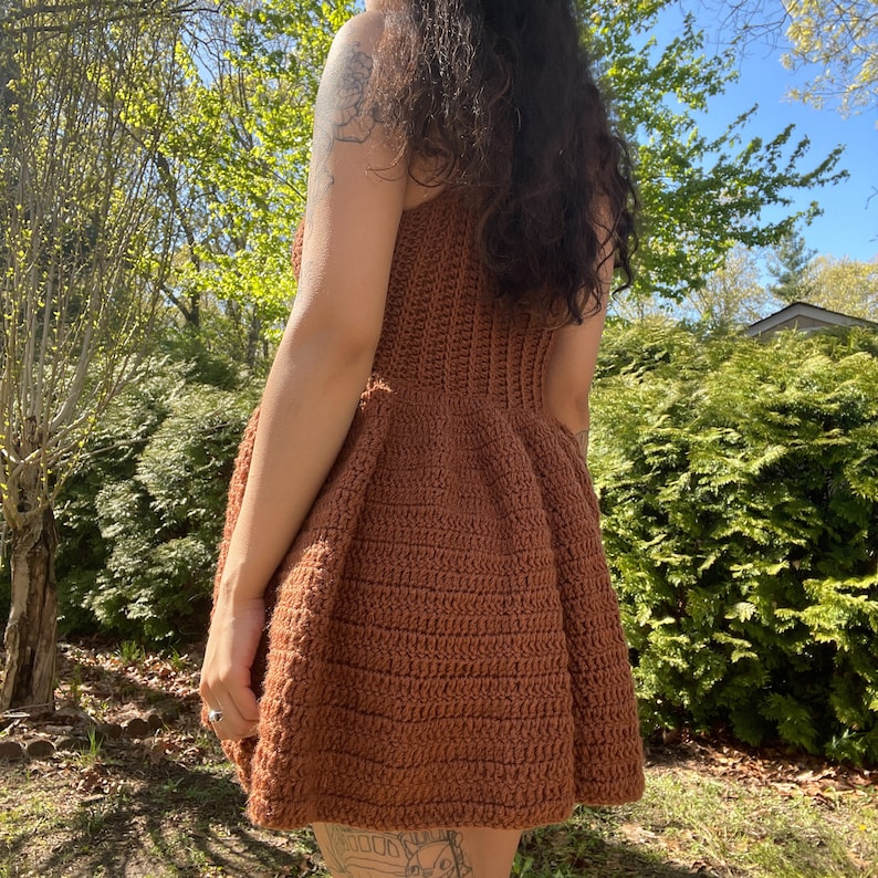 May include: A brown crochet dress with a fitted bodice and a flared skirt. The dress is made with a simple stitch pattern and has a casual, bohemian style.