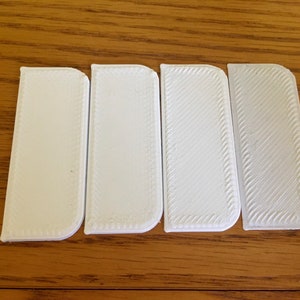May include: Four white plastic rectangular shapes with rounded corners. The first two shapes are smooth, while the last two have a textured surface.