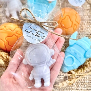 May include: A small, clear plastic bag filled with a lavender astronaut-shaped soap. The bag is tied with twine and a small round tag that reads "Hope you had a blast - Theodore".