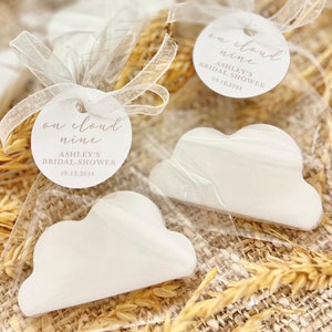 May include: White cloud-shaped favors with a round tag that says "on cloud nine" Ashley's Bridal Shower 09.12.2024.