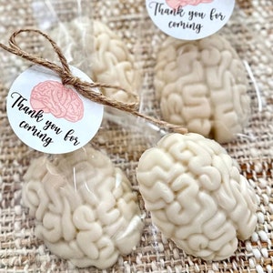 May include: White brain-shaped favors in clear plastic bags with a pink and white thank you for coming tag tied with twine.