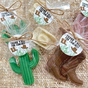 May include: A set of four favor bags with different cowboy-themed treats. Each bag is tied with twine and includes a round tag that says "Thank Y'all for Coming!" with a cowboy hat and boots graphic. The treats include a cactus, a cowboy hat, and cowboy boots.