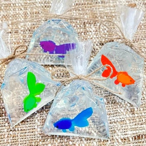 May include: Four clear plastic bags tied with twine, each containing a colorful fish-shaped soap. The soaps are purple, green, blue, and orange.